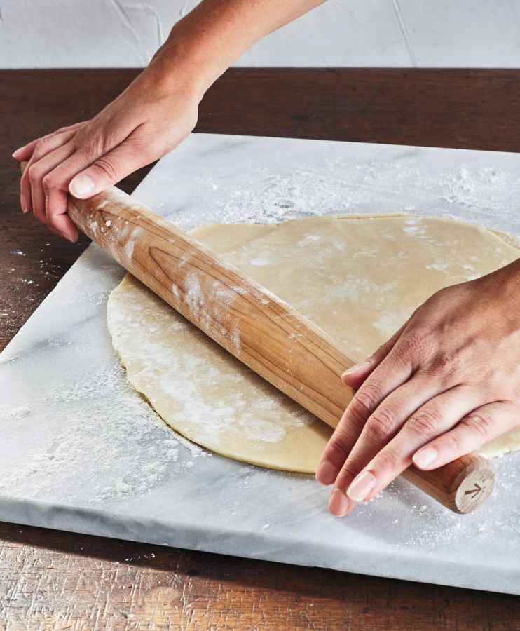 tapered wooden rolling pin rolling out pastry on marble board