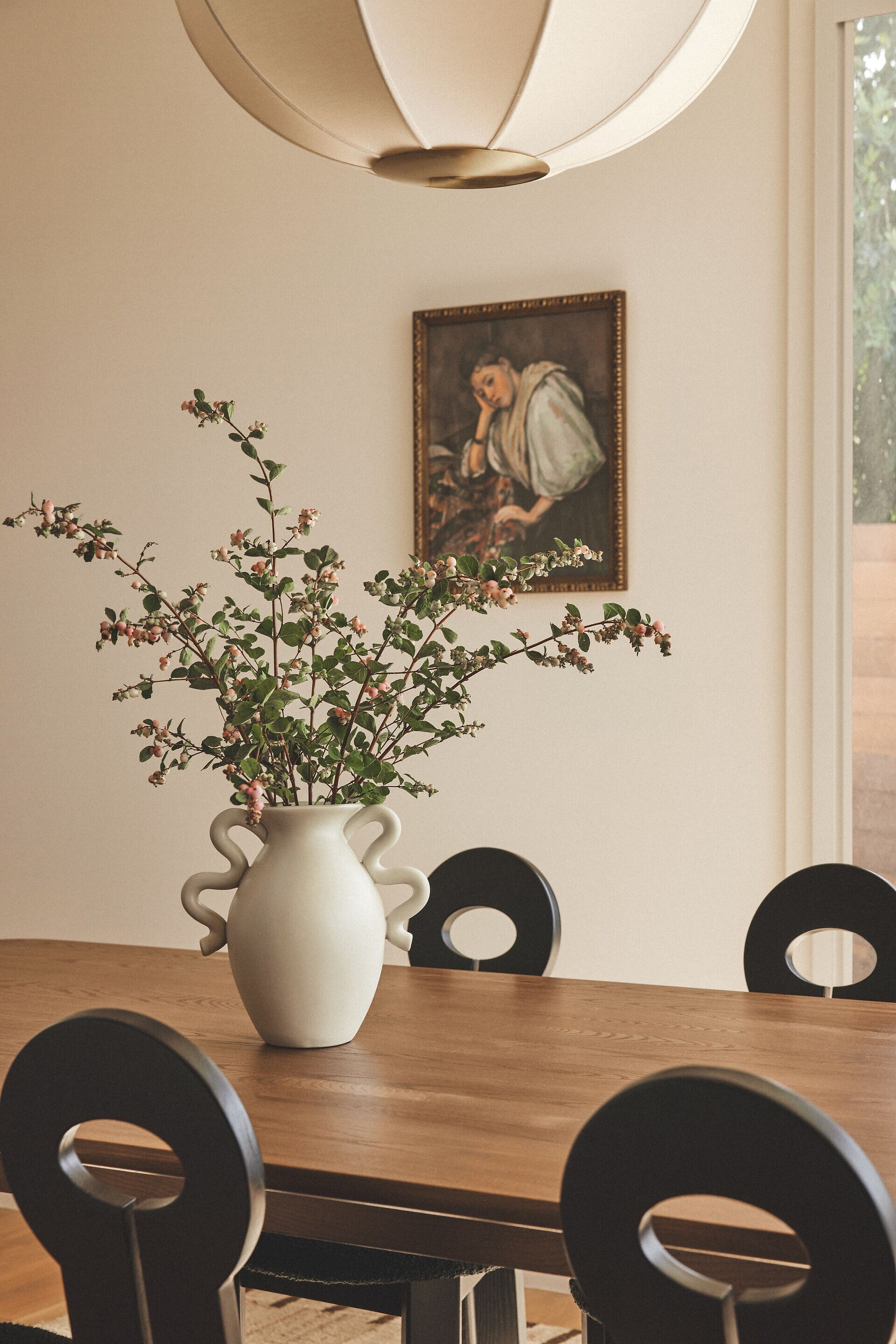 Modern dining room with a circular table, artistic chairs, a large pendant light, and a religious painting on the wall
