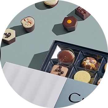 An assortment of fine chocolates in a box, some are unwrapped, on a gray surface