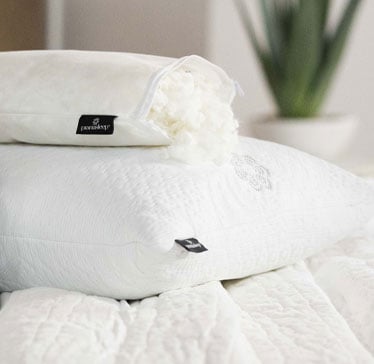 White pillows with tags on a bed, decorated with a white flower, in a softly lit room