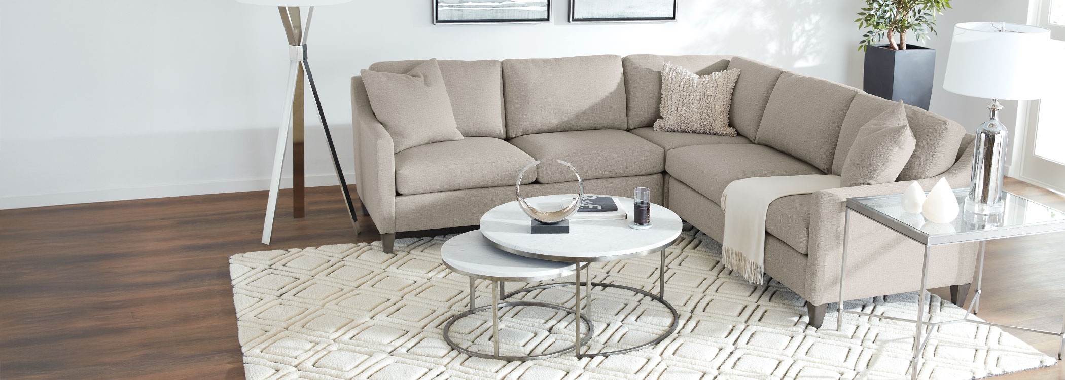 Modern living room with beige sectional sofa, white round coffee table, and wooden floor