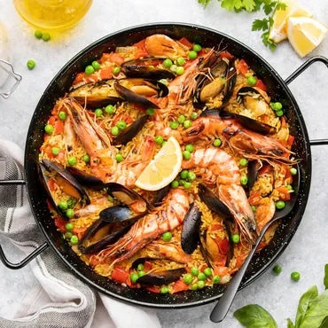 A pan of seafood paella with shrimp, mussels, peas, and lemon slices
