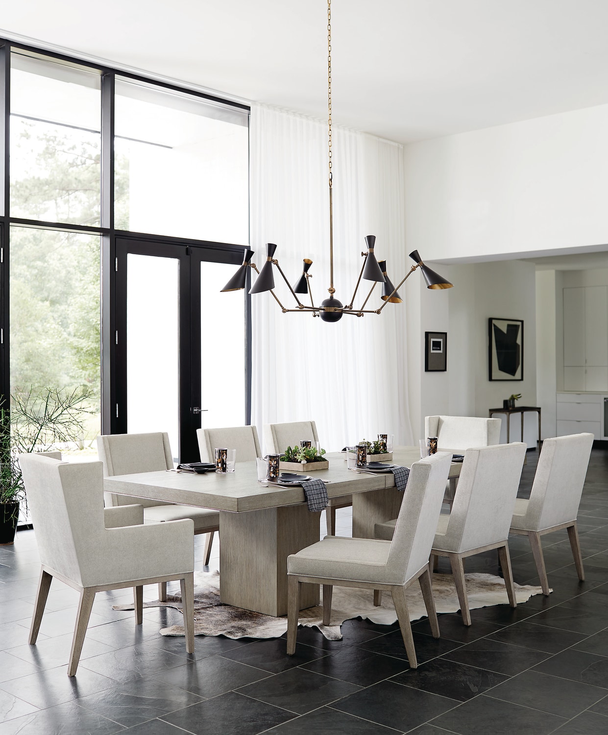 Modern dining room with a large table, eight chairs, and a geometric chandelier, surrounded by large windows