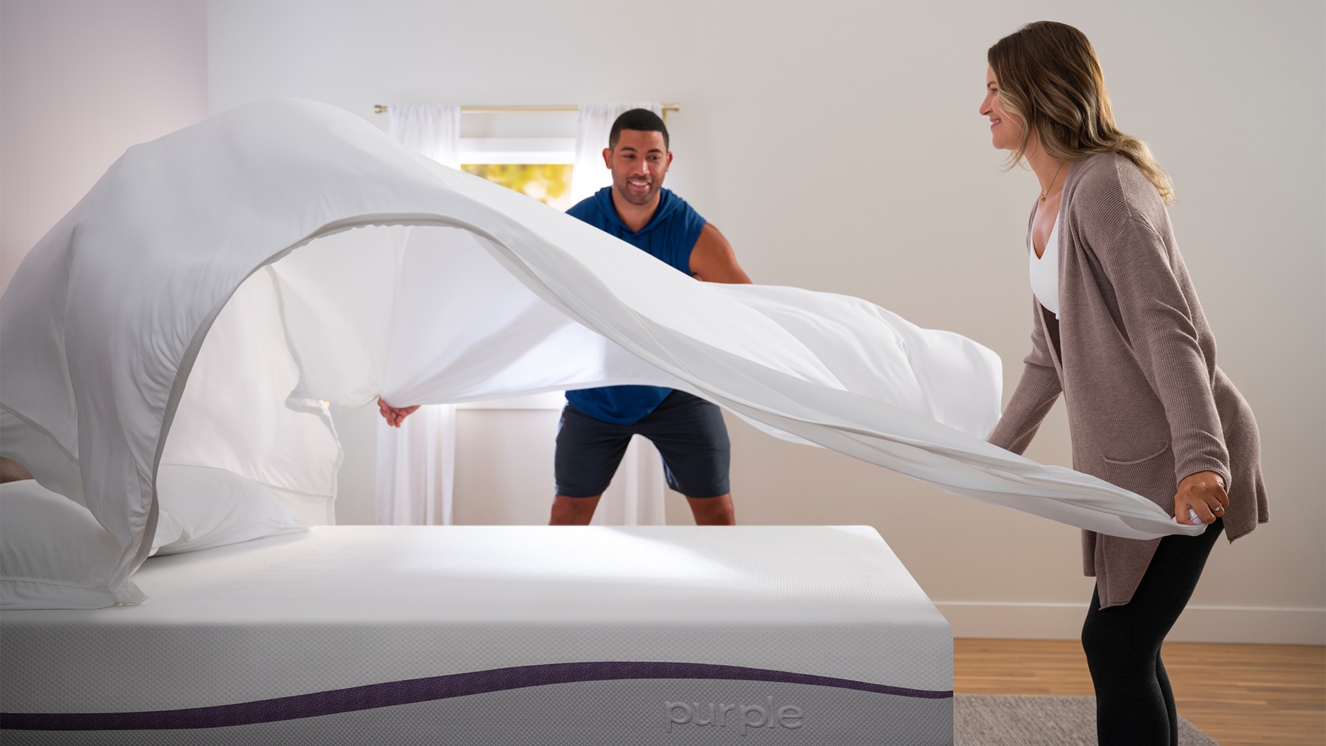 A man and a woman making a bed together, smiling as they spread a white sheet