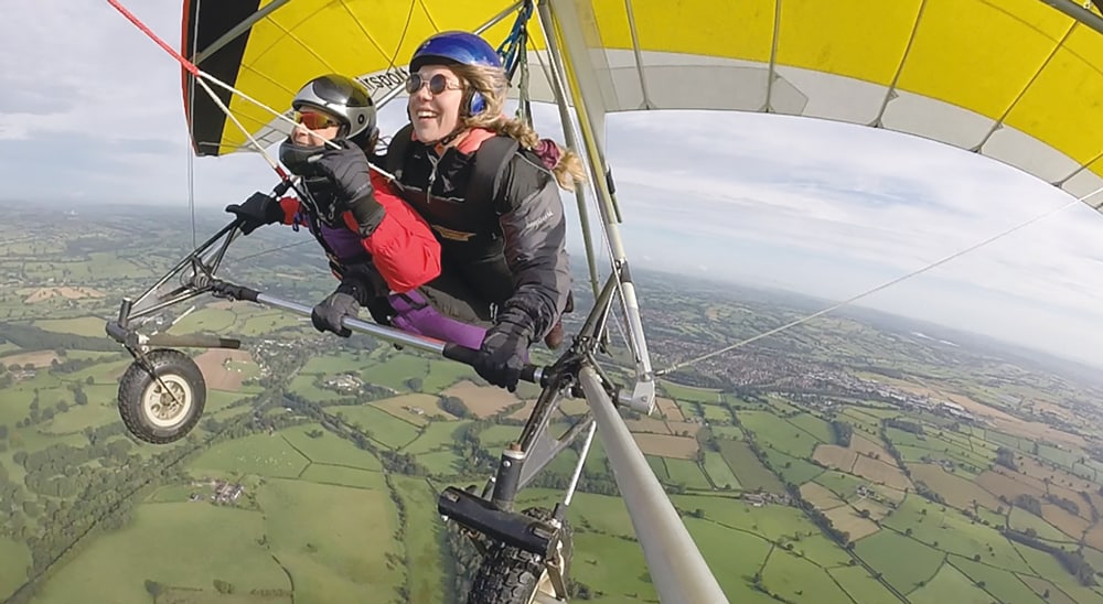 Deux personnes souriantes faisant du deltaplane au-dessus d'un paysage verdoyant