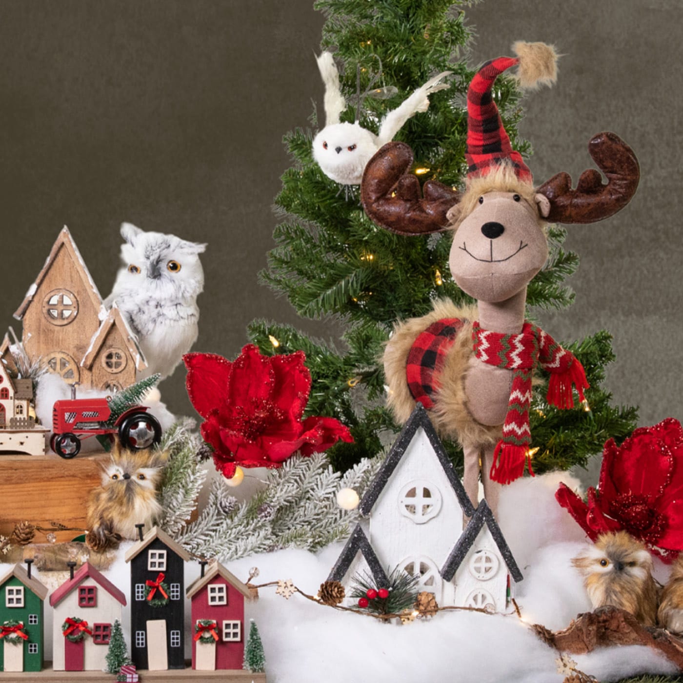 Christmas display with a reindeer doll, snowy village, owls, and red flowers