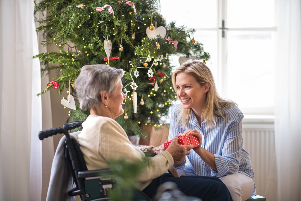 Young woman giving a gift to an elderly woman by a Christmas tree.