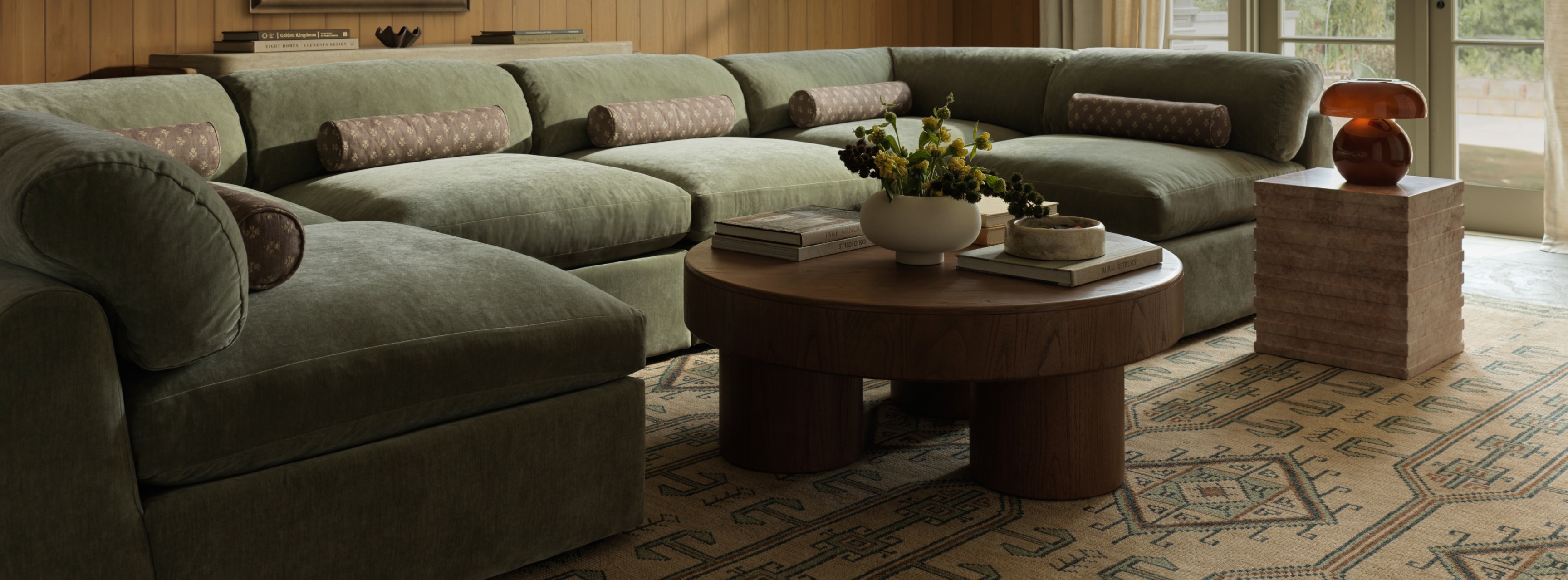 A spacious living room with a large, curved grey sofa and a round wooden coffee table