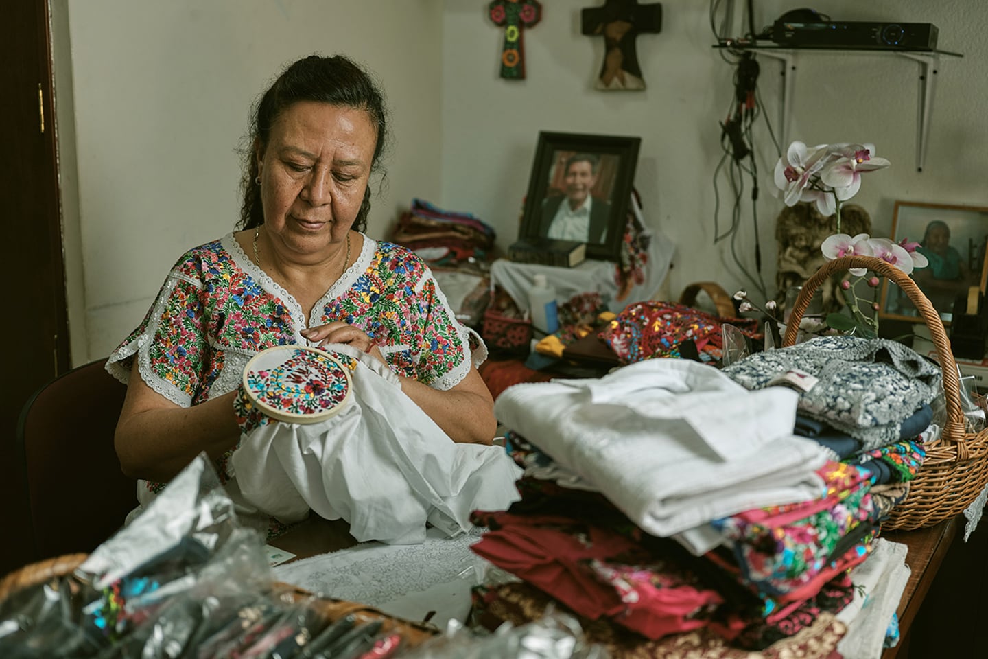 A woman sewing in a room surrounded by baskets of colorful fabrics and textiles
