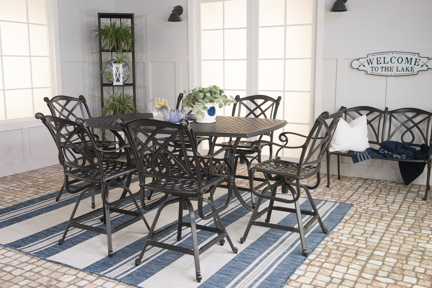 Elegant patio setup with a wrought-iron dining set and striped rug under a shaded veranda