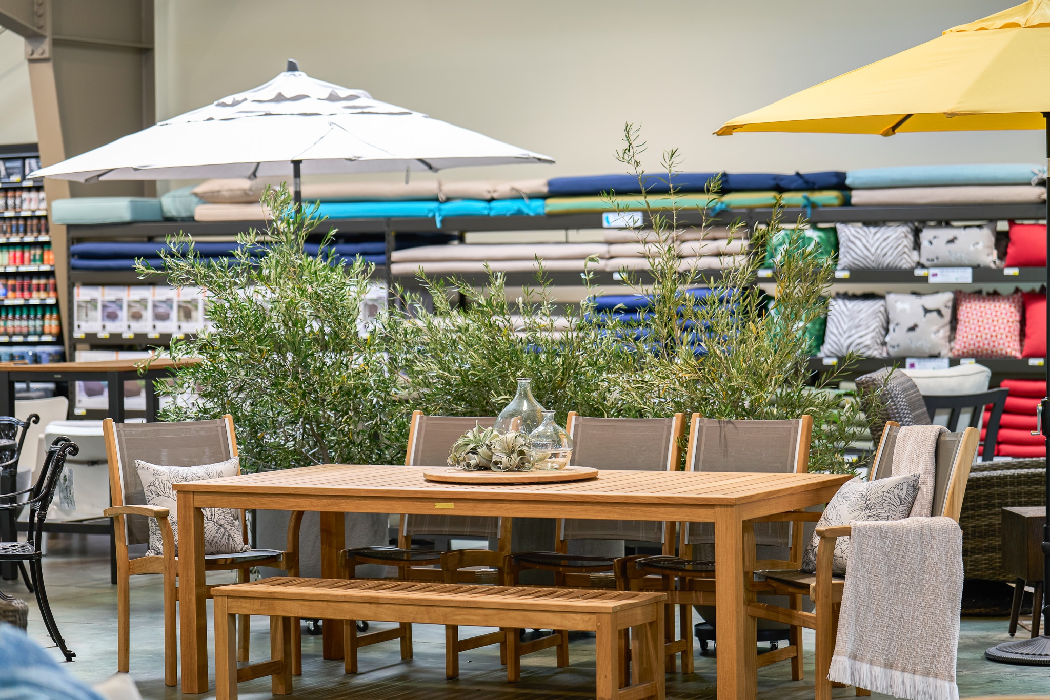 Outdoor furniture display with a wooden table and chairs under store umbrellas