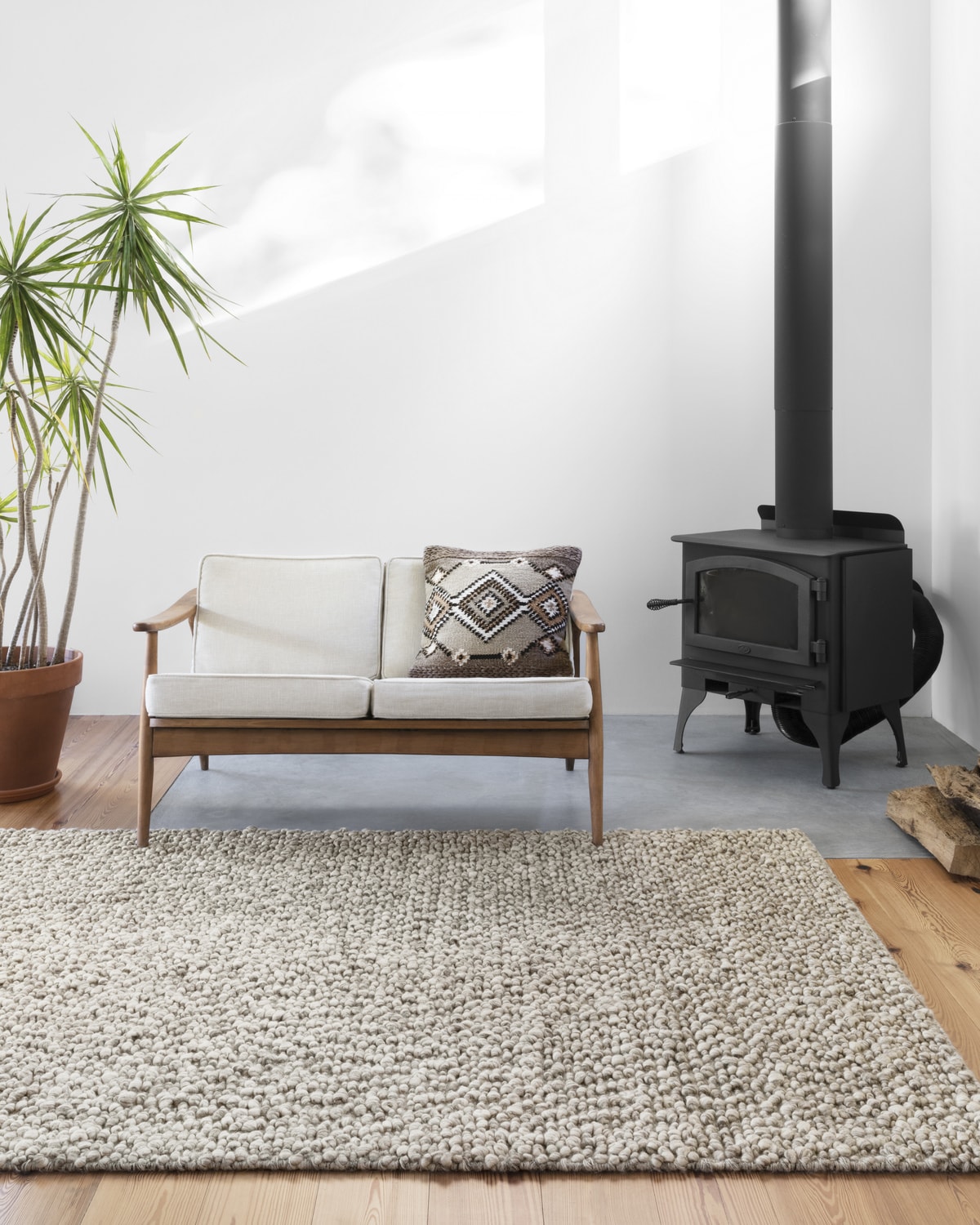 Modern living room with a wooden sofa, wood stove, white rug, and a potted plant
