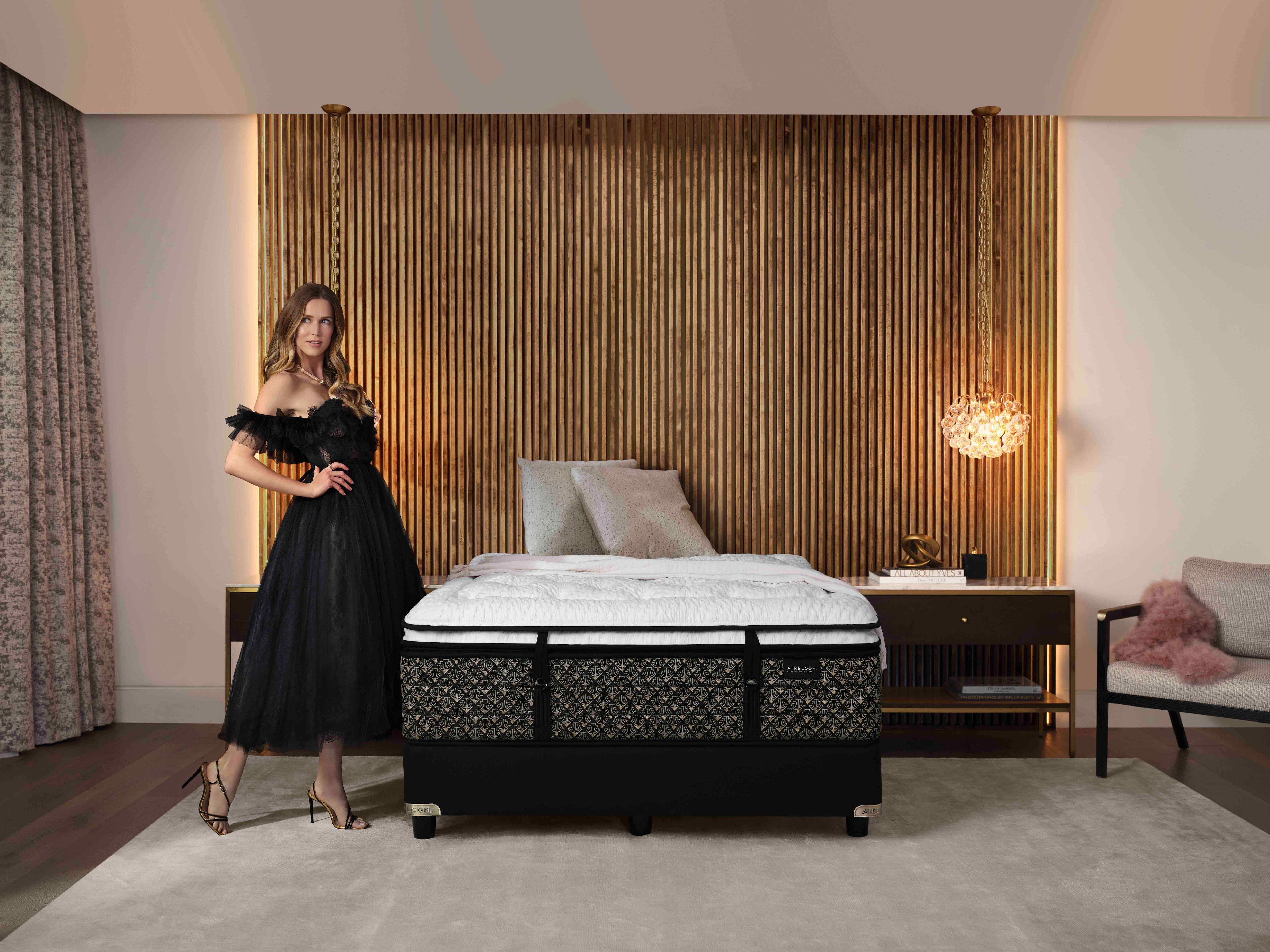 Woman in black dress standing beside a bed in a stylish bedroom