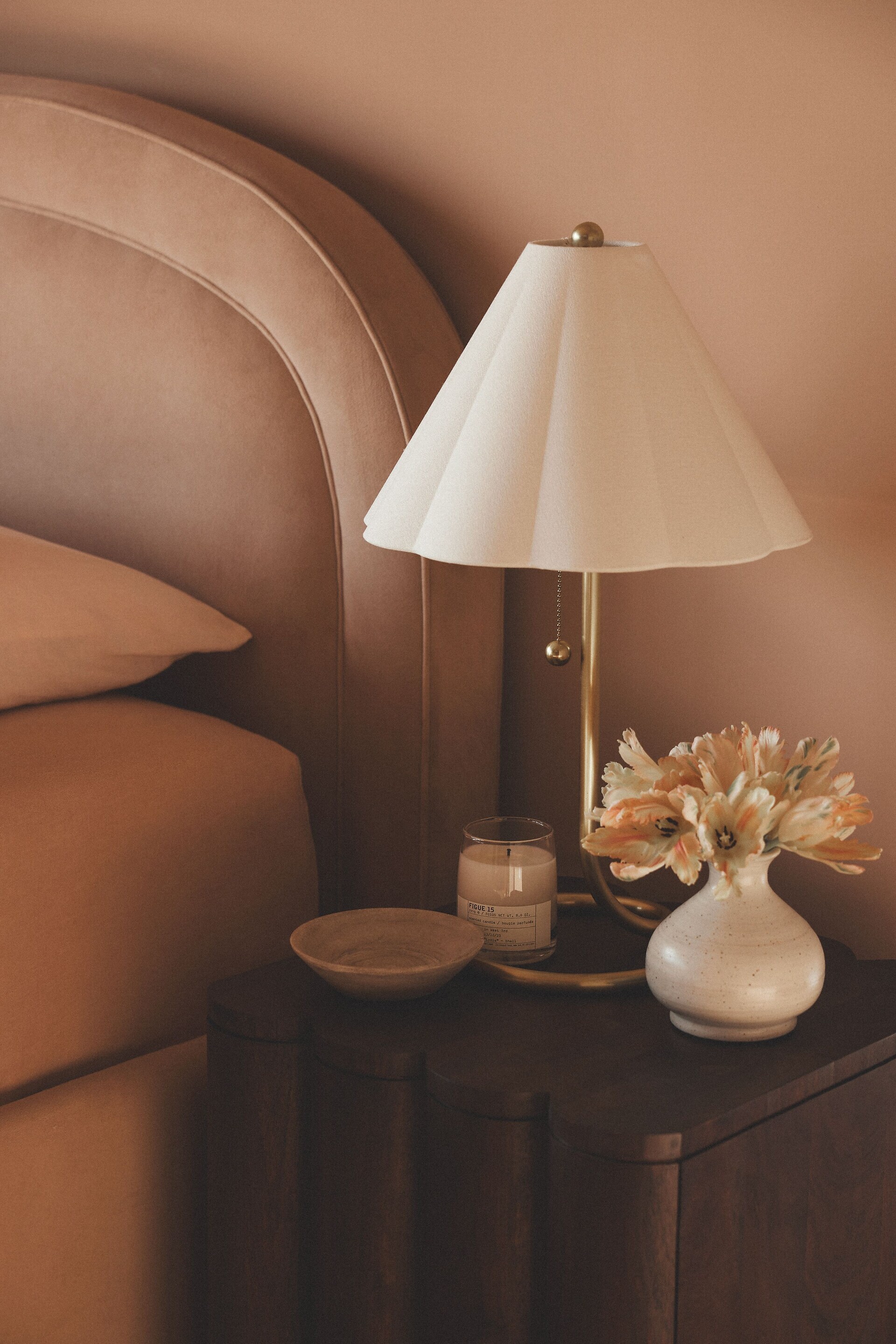 A cozy corner with a lamp, flowers in a vase, and aromatic candle on a bedside table
