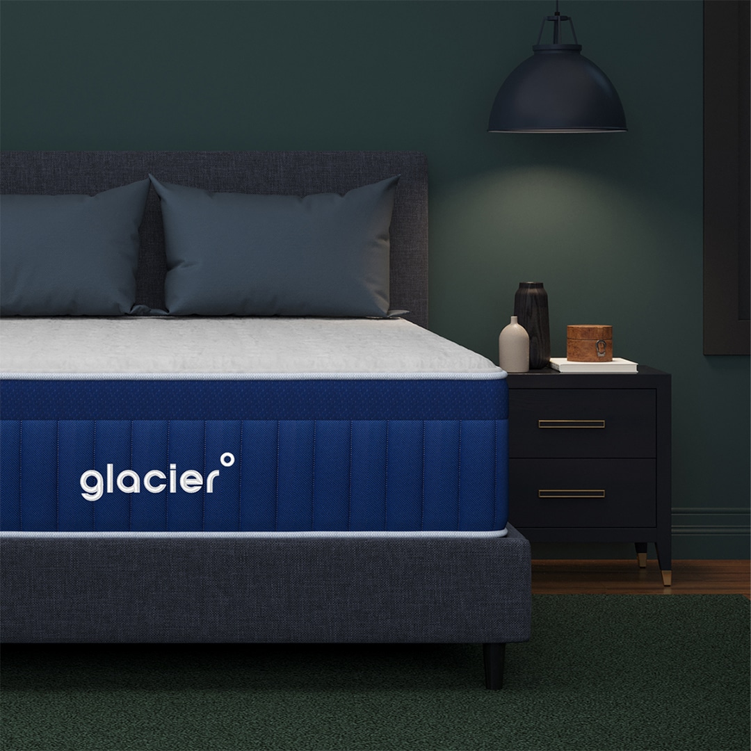 A bedroom with a dark green wall, featuring a bed with Glacier mattress and a black bedside table