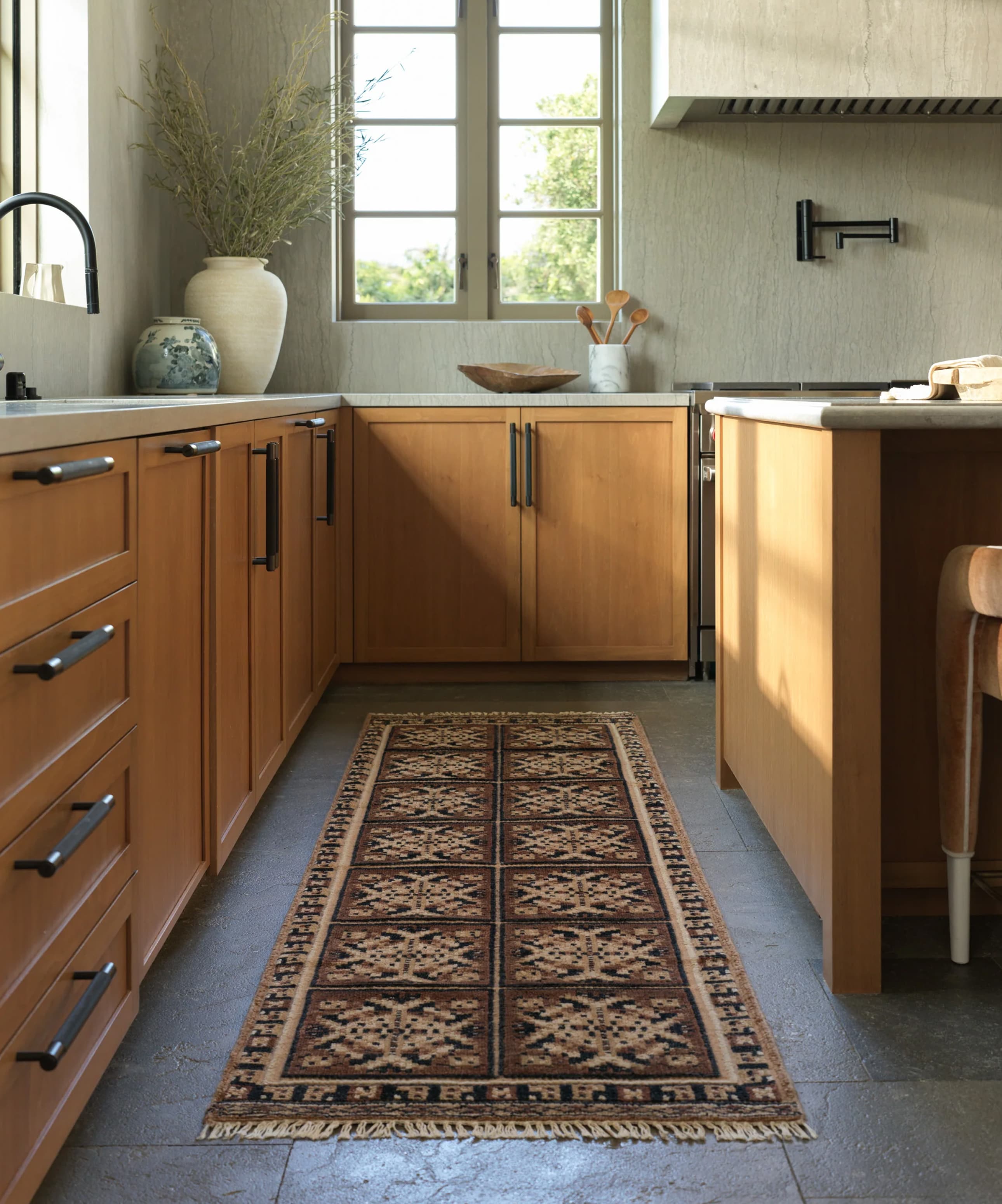 Modern kitchen with wooden cabinets, a patterned rug, and stainless steel appliances