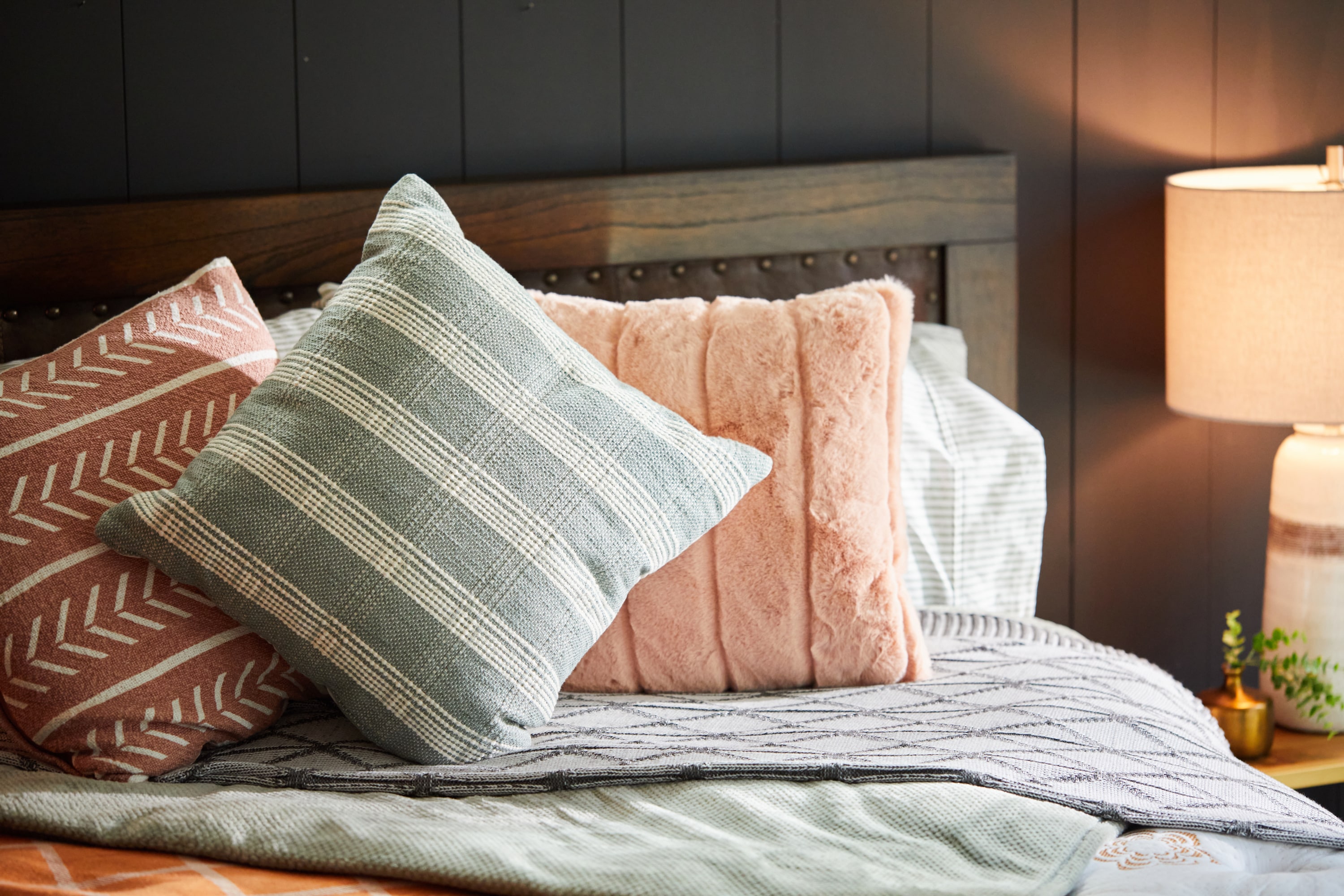 Cozy bedroom with decorative pillows on a bed, a lit bedside lamp, and dark paneled wall