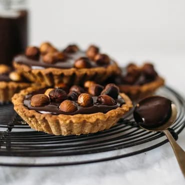 Chocolate hazelnut tarts on a cooling rack with a spoonful of chocolate spread