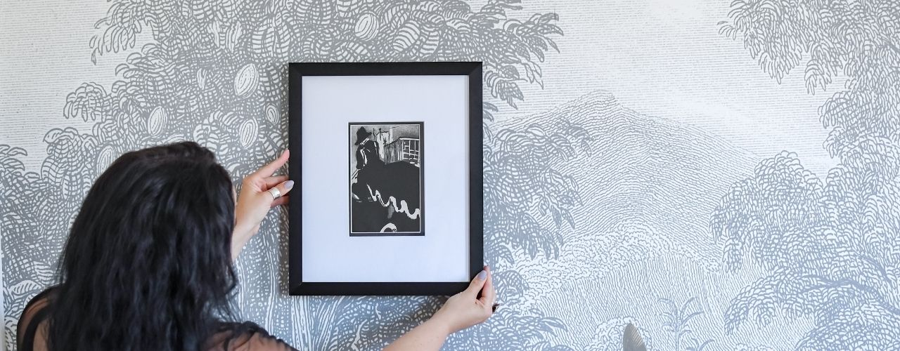 Woman hanging a framed picture on a patterned wall