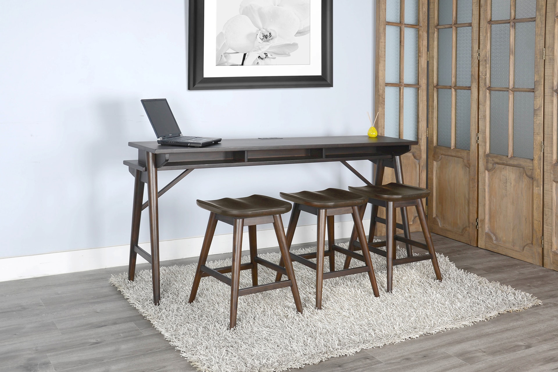 Modern home office with a dark wooden desk, four stools, and a laptop, set against a blue wall with artwork