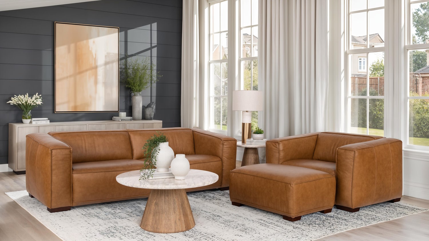Modern living room with brown leather sofas, round wooden coffee table, large window, and decorative plants
