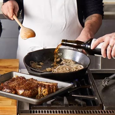 Chef pouring sauce from pan onto dish with ribs, in a professional kitchen