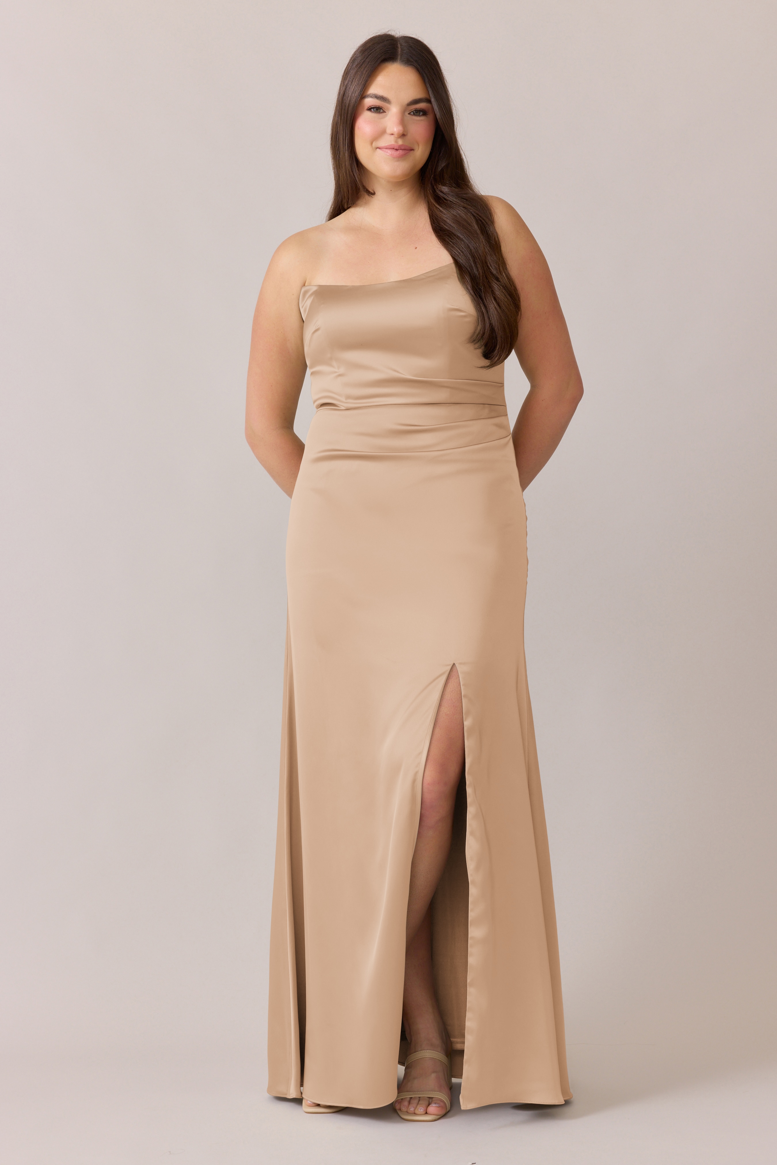 Woman in a beige sleeveless gown with a slit, posing against a gray background