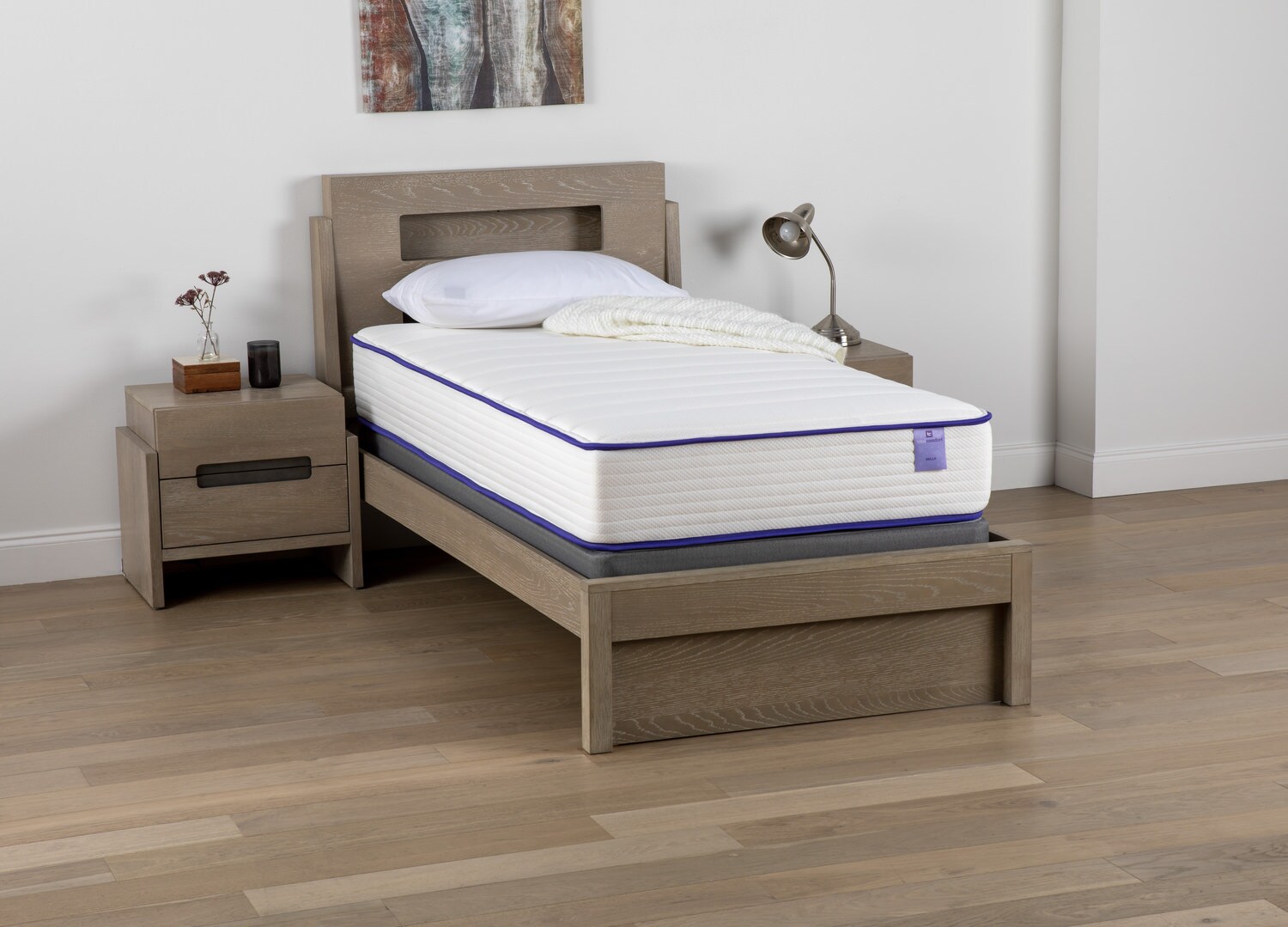 Single bed with a white and blue mattress on a wooden bed frame, next to a matching nightstand in a room with hardwood flooring