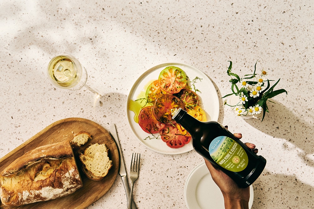 Top-down view of a meal with shrimp pasta, bread, white wine, and a hand pouring beer from a bottle