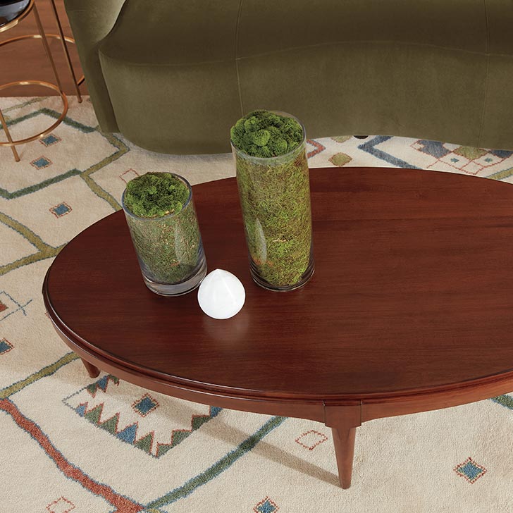 Two green vases on a wooden oval coffee table in a room with patterned rug