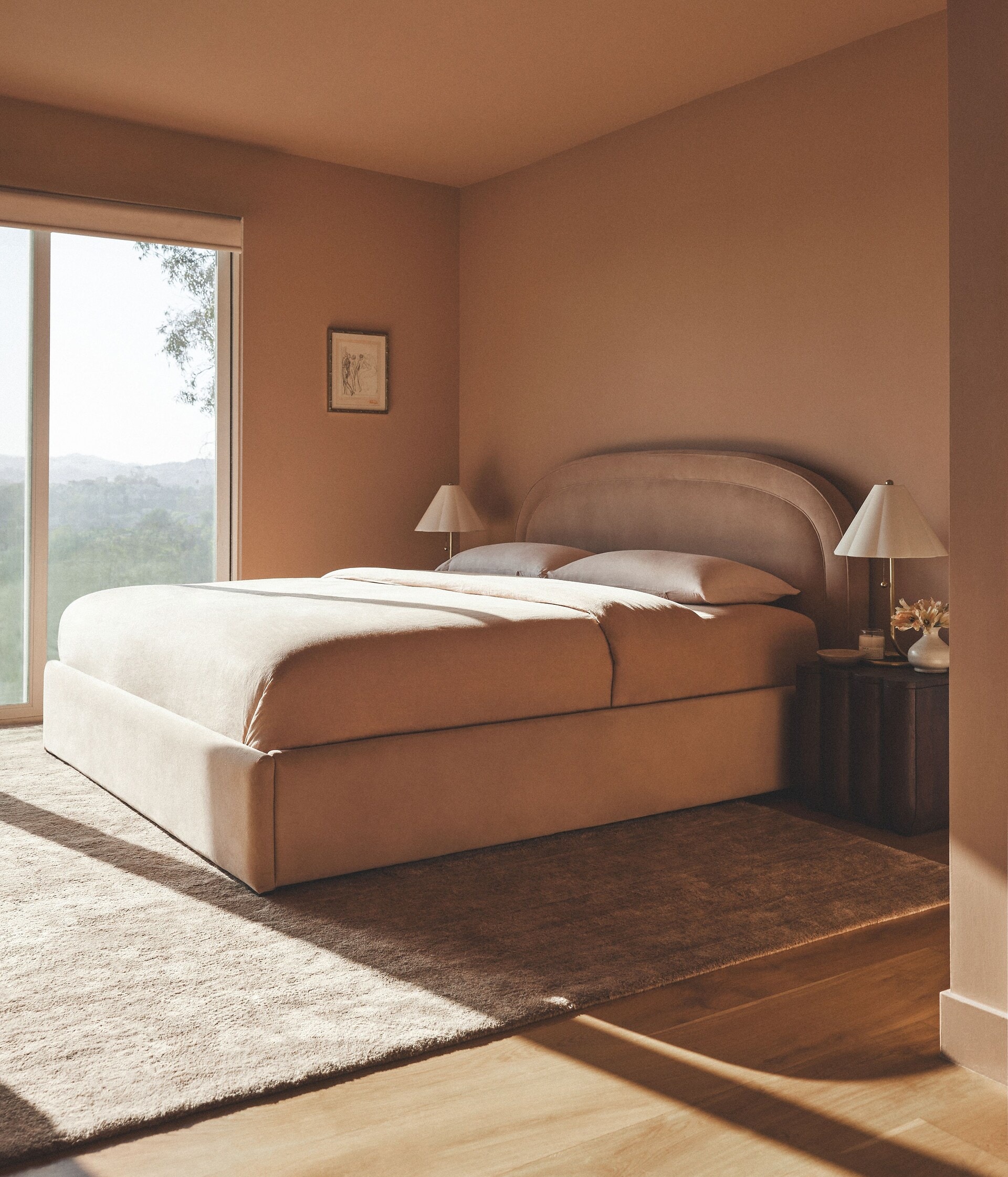 Minimalist bedroom with a large bed and open window overlooking green hills