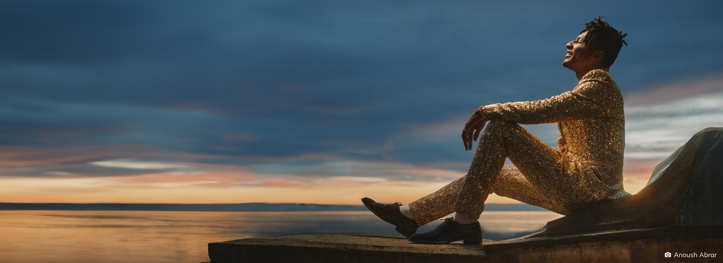 Man sitting on a rock by the sea at sunset, looking contemplative