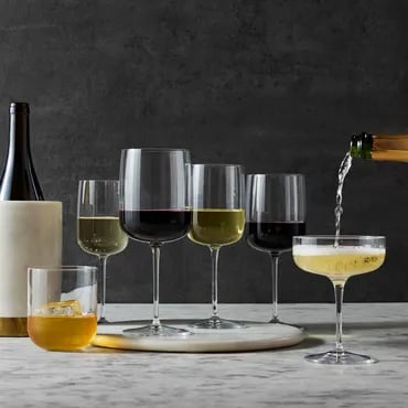 Wine being poured into a glass, with multiple glasses of red and white wine arranged on a table