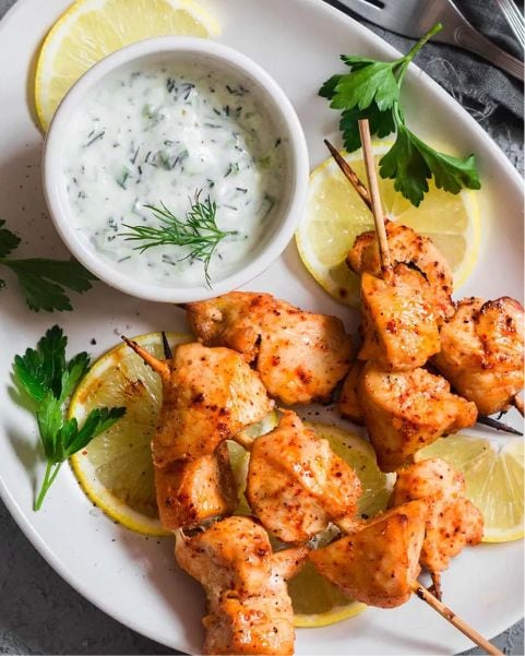 chicken on skewers with sauce on an oval plate