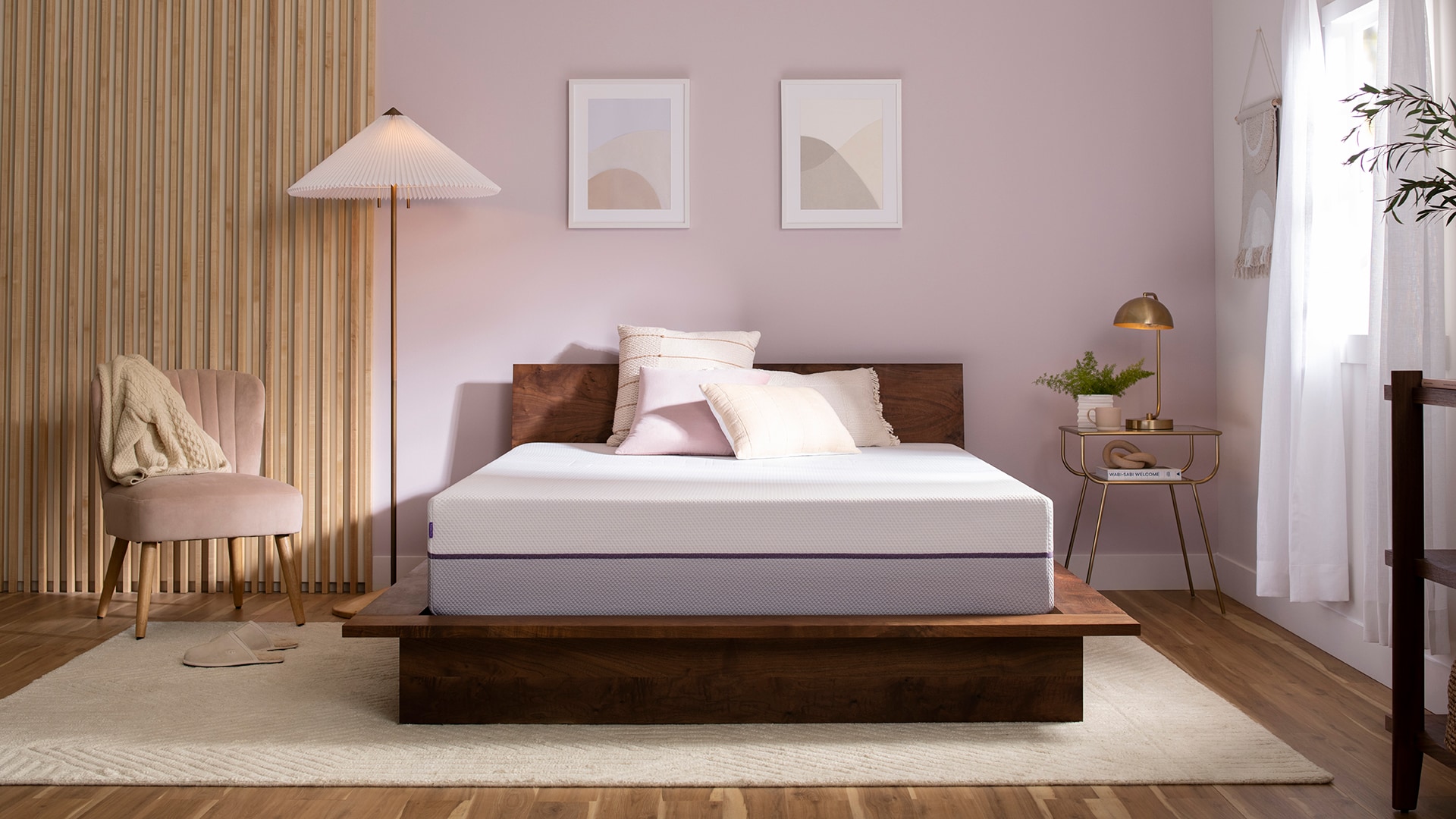 Modern bedroom with a large bed, peach walls, wooden floor, and minimalist decor including a chair and side table