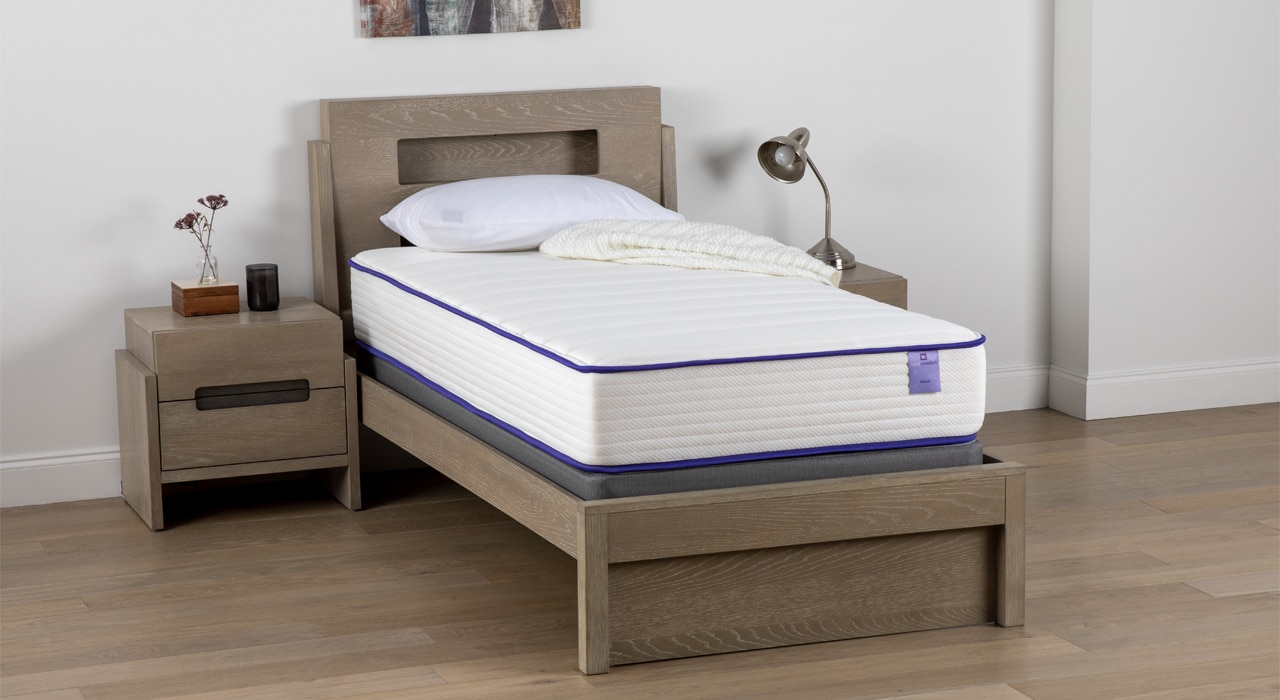 Single bed with mattress in a room with a wooden nightstand and a lamp