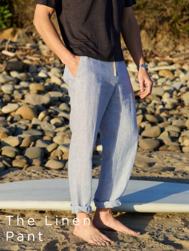 Man in black t-shirt and linen pants standing on a beach, surfboard visible. Text: "The Linen Pant