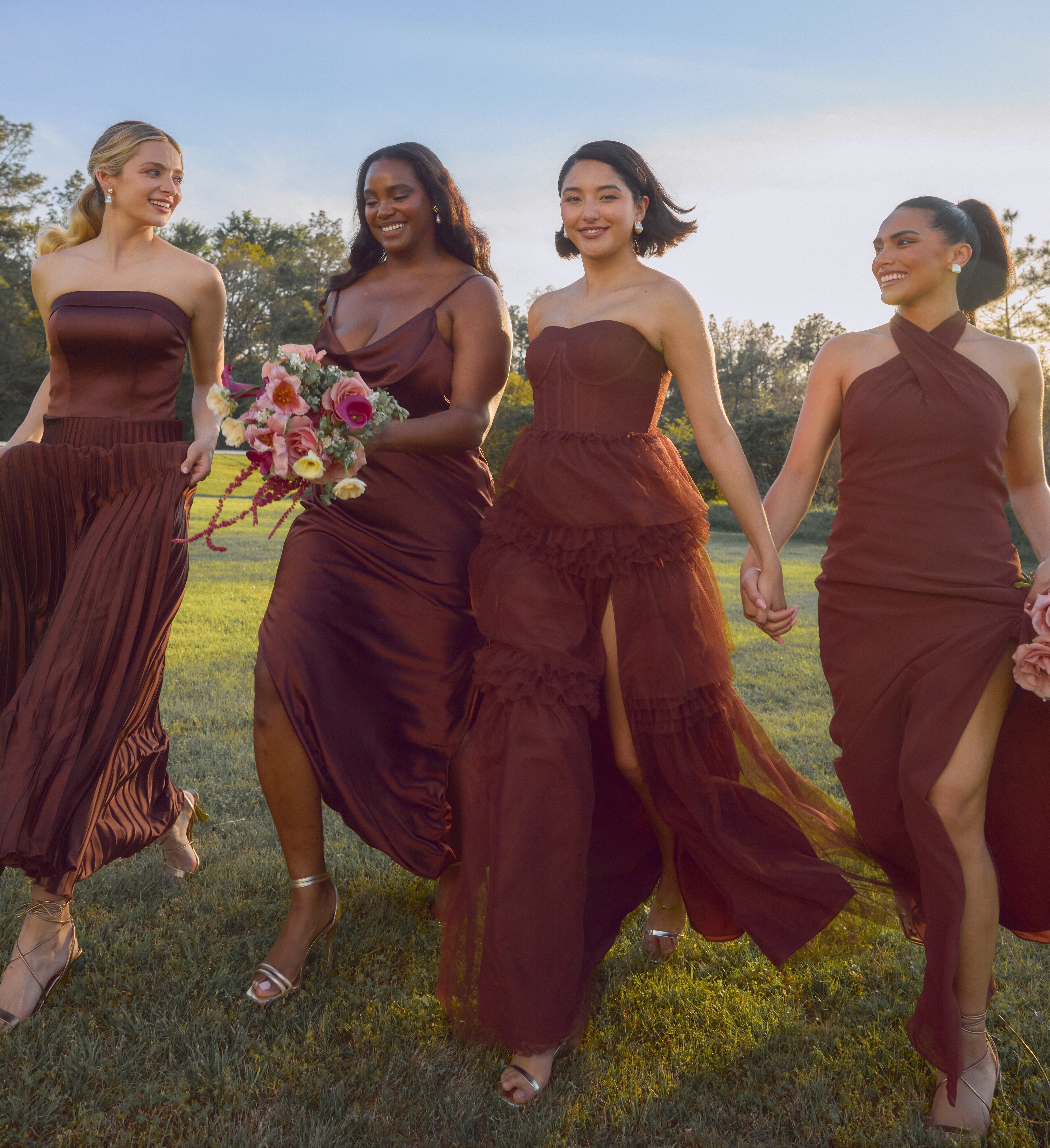 Four bridesmaids in matching burgundy dresses walking joyfully on grass