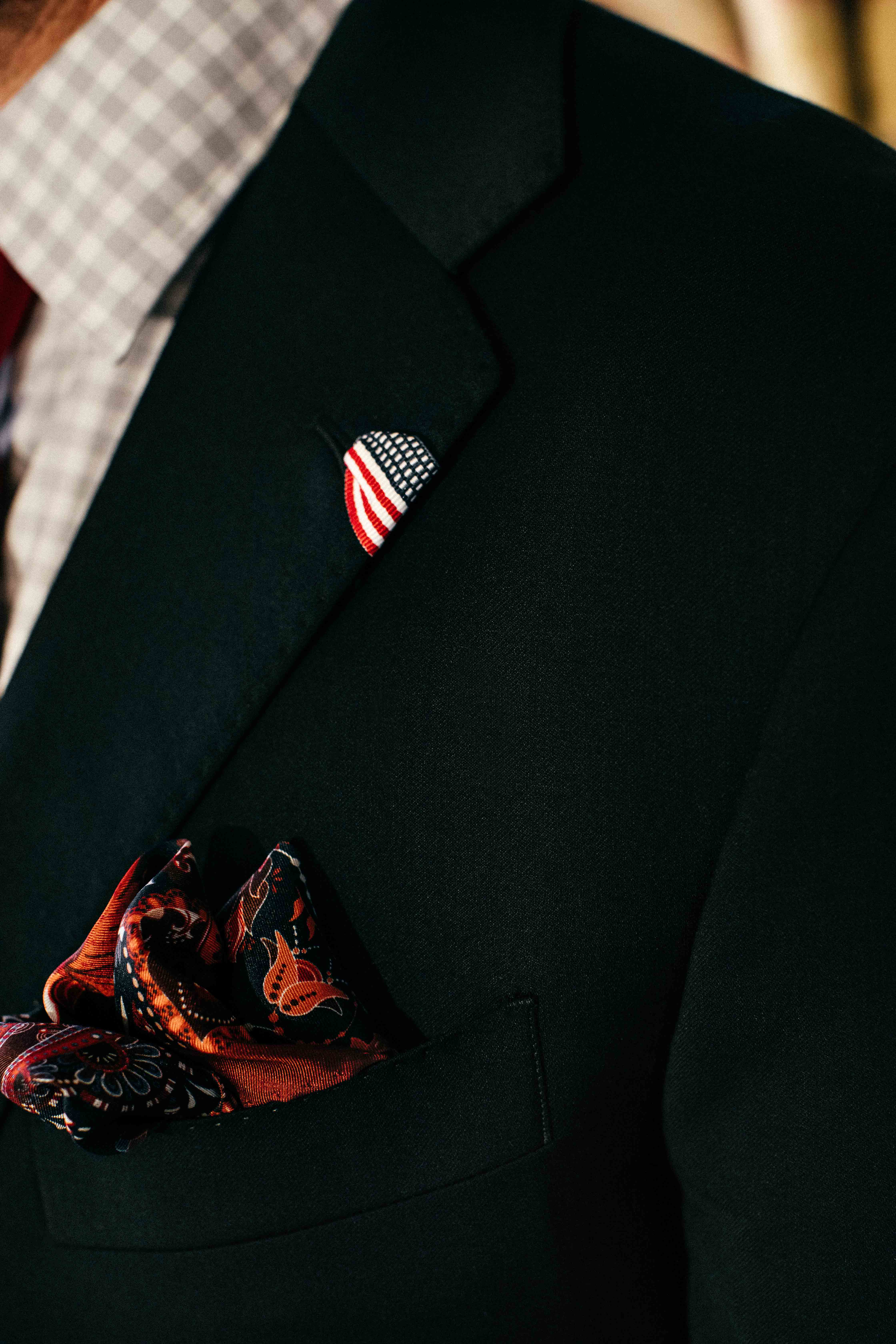 Close-up of a dark suit jacket with an American flag pin and a patterned pocket square