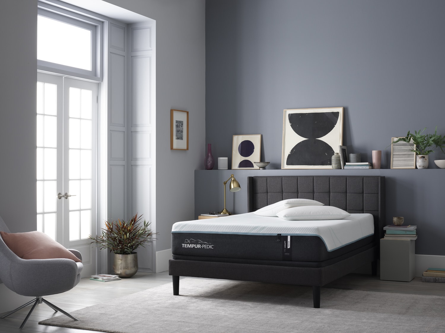 Modern bedroom with a gray tufted bed, a chair, plants, and minimal decor