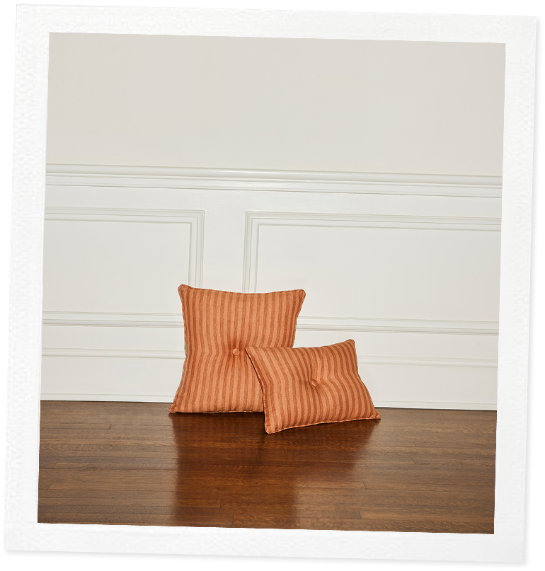 Two orange striped pillows on a wooden floor against a white paneled wall