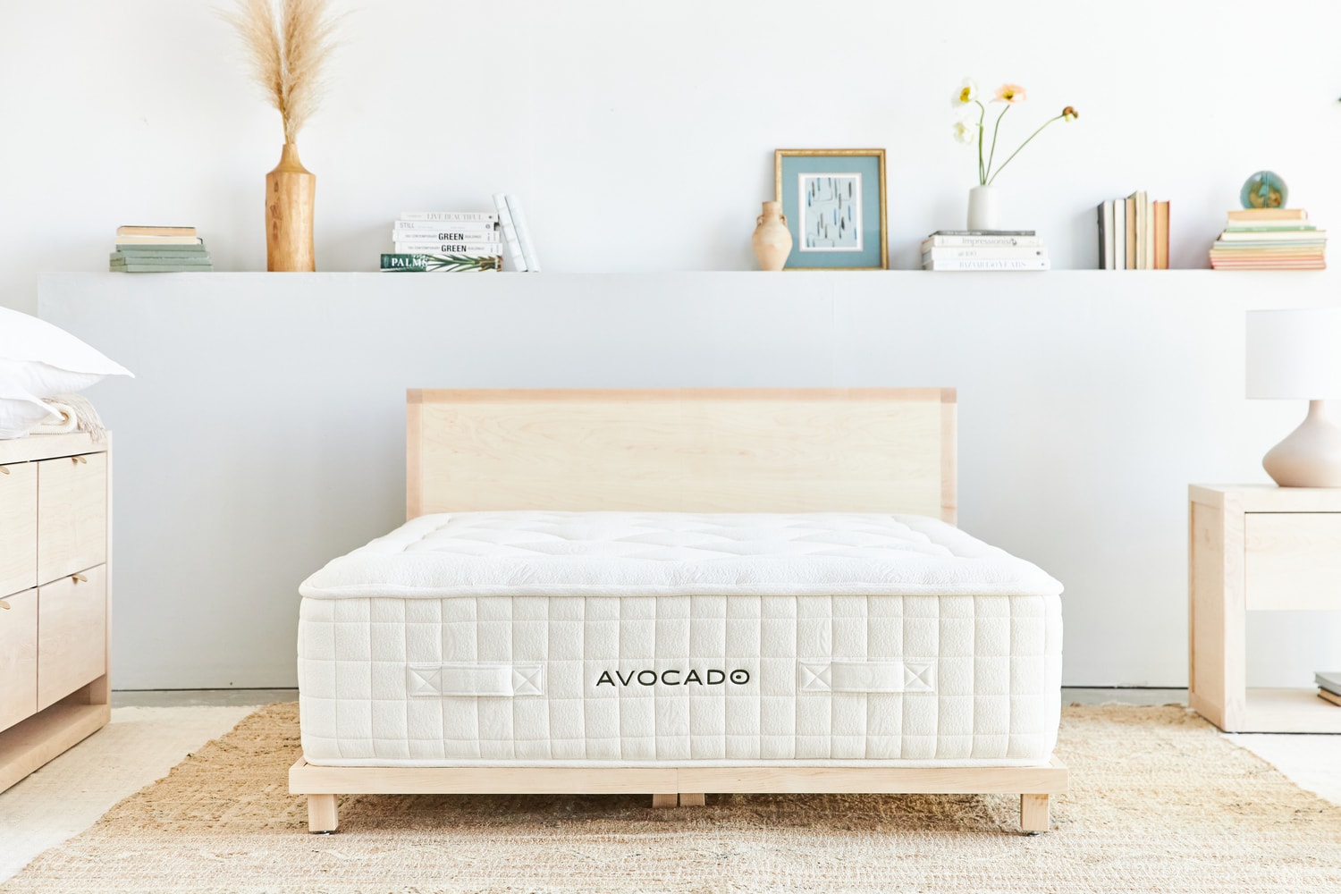 Modern bedroom with a wooden bed frame, white mattress labeled 'Avocado,' and minimalist decor on a floating shelf