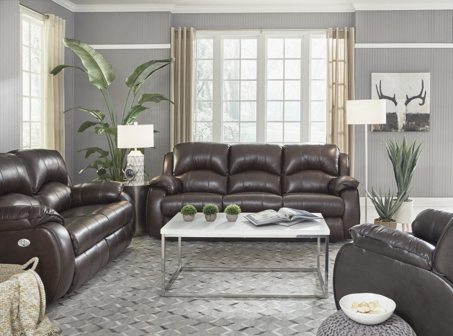 Elegant living room with brown leather sofas, a white coffee table, and gray walls decorated with plants and artwork