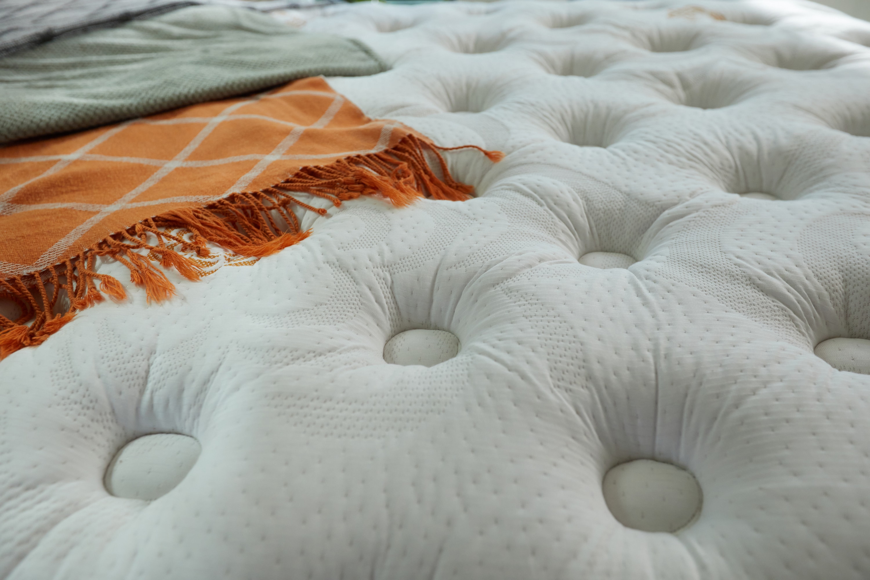 Close-up of a white tufted mattress with an orange plaid blanket