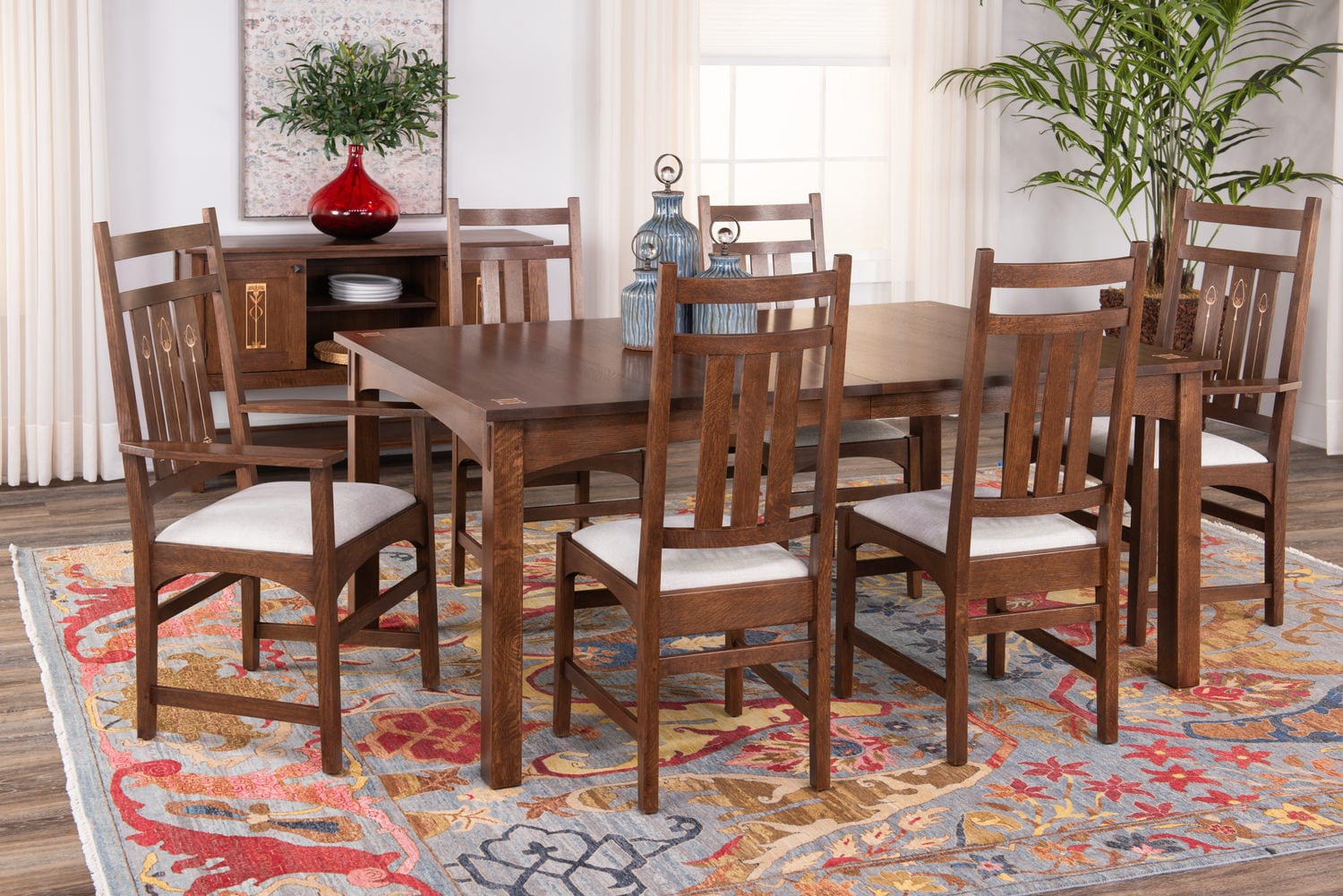 Wooden dining table set with eight chairs in a room with plants and a colorful rug