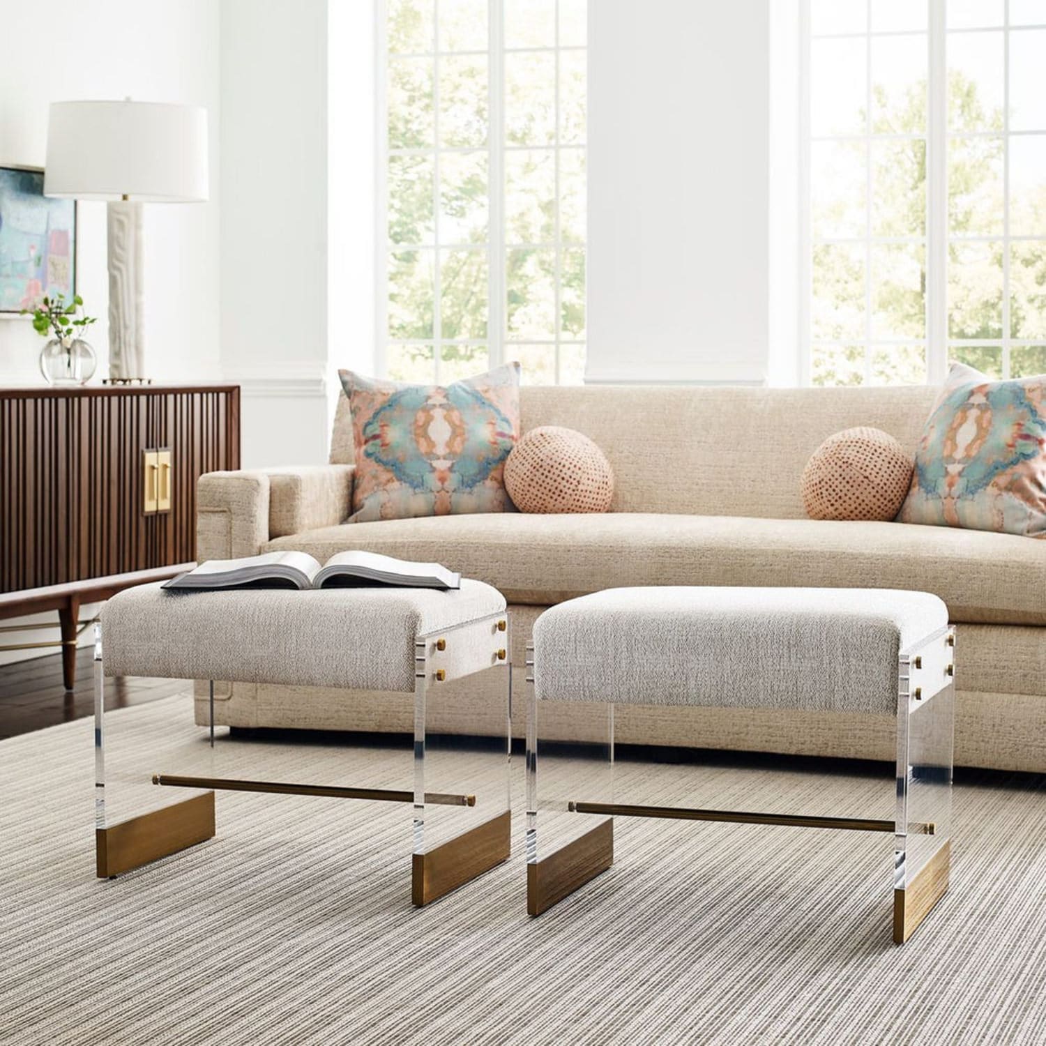 Modern living room with beige sofa, two stools, and large windows