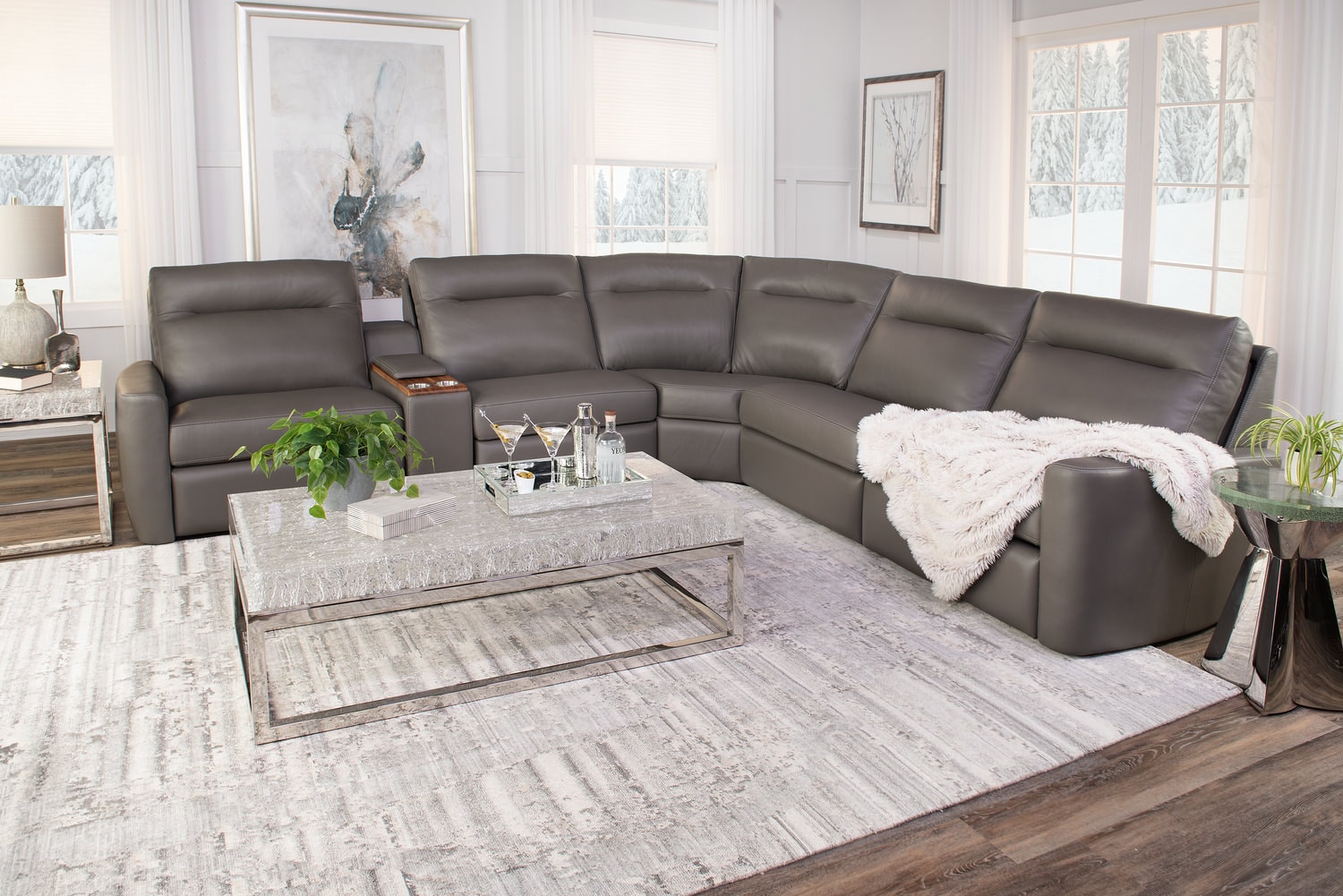 Modern living room with a large gray sectional sofa, a white rug, glass coffee table, and light-filled windows