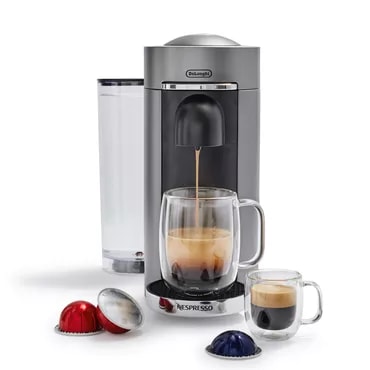 A single-serve coffee maker with a capsule, dispensing coffee into a mug, surrounded by more capsules and a glass