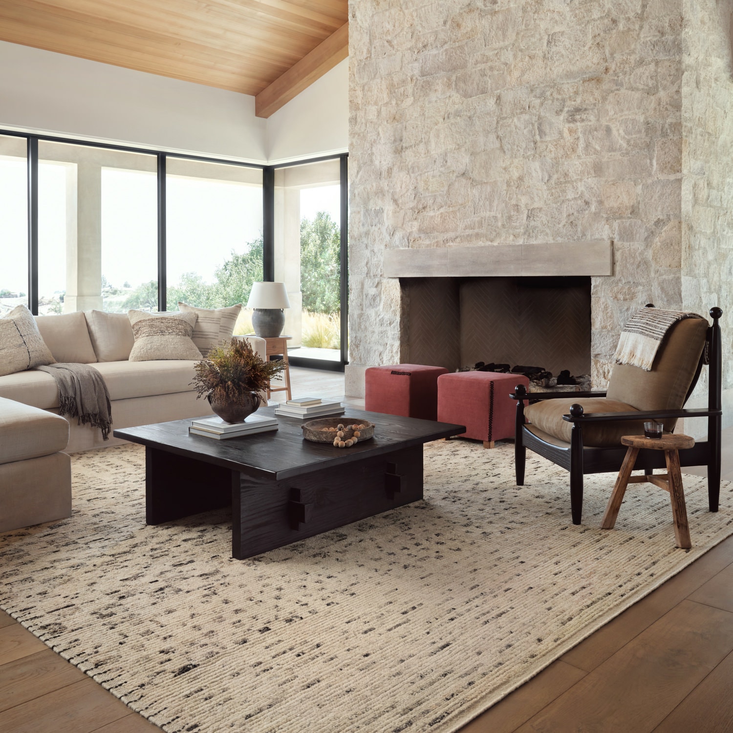 Modern living room with a stone fireplace, large windows, a beige sofa, and wooden coffee table