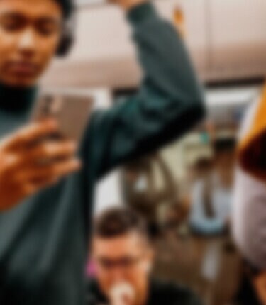 Man in headphones using smartphone, two others working in background